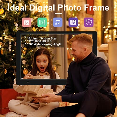 Man and girl looking at digital photo frame near Christmas tree.