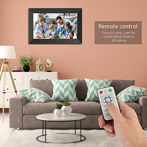 Hand holding remote control in front of digital photo frame on wall above sofa.