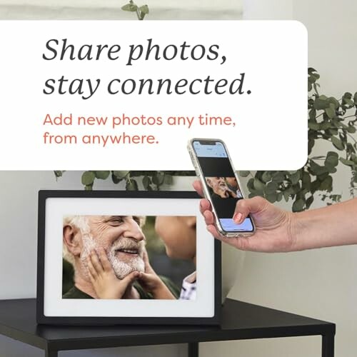 Digital photo frame with a hand holding a phone, displaying a smiling elderly man and child.